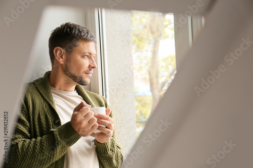 Man with cup of tea relaxing near window at home photo