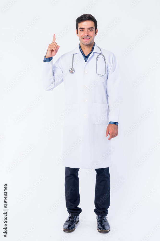 Full body shot of happy young Persian man doctor pointing up Full body shot of happy young Persian man doctor pointing up