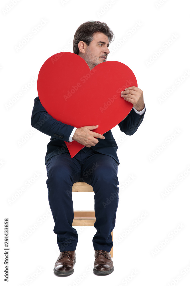 businessman sitting and holding a big red heart looking sideways