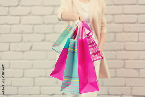 Female hands holding flowers and shopping bags on brick background. Woman's day. Valentine's day. Ready for birthday party. Copy space. Bunch of paper gift bags