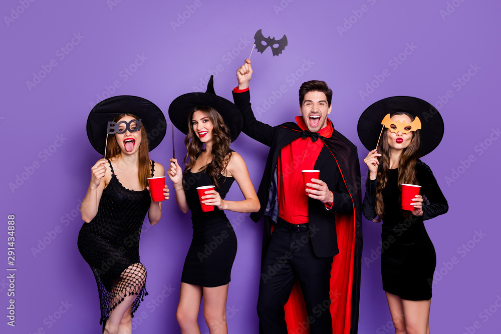 Photo of three witch ladies and wizard guy at halloween party drink beer wear stick masks black dresses hats suit and long coat isolated purple color background