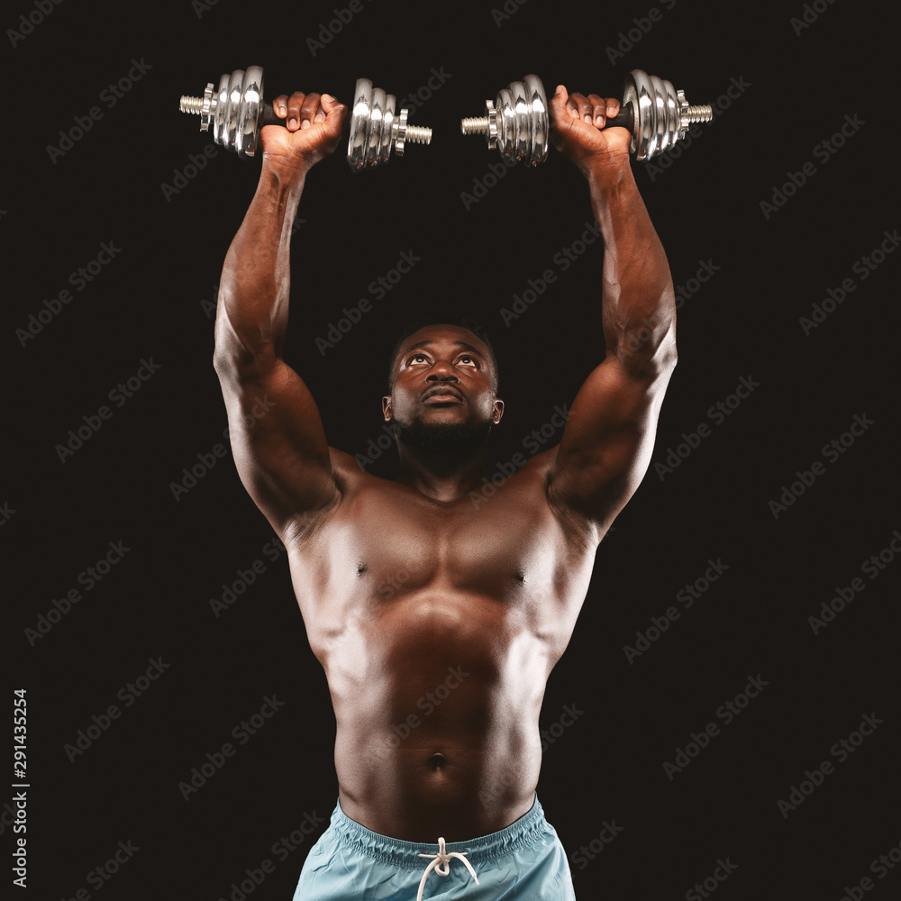 Hot bodybuilder lifting dumbbells up over black background Hot bodybuilder lifting dumbbells up over black background