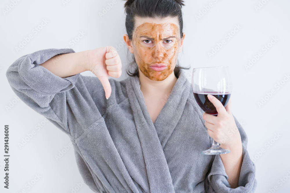 Beautiful woman wearing cosmetic facial mask as skincare treatment drinking glass of wine with angry face, negative sign showing dislike with thumbs down, rejection concept Beautiful woman wearing cosmetic facial mask as skincare treatment drinking glass of wine with angry face, negative sign showing dislike with thumbs down, rejection concept