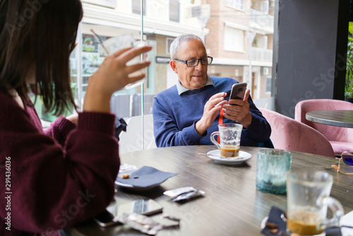 Senior man having a conversation with woman drinking coffee using smartphone and relaxing, chatting at restaurant