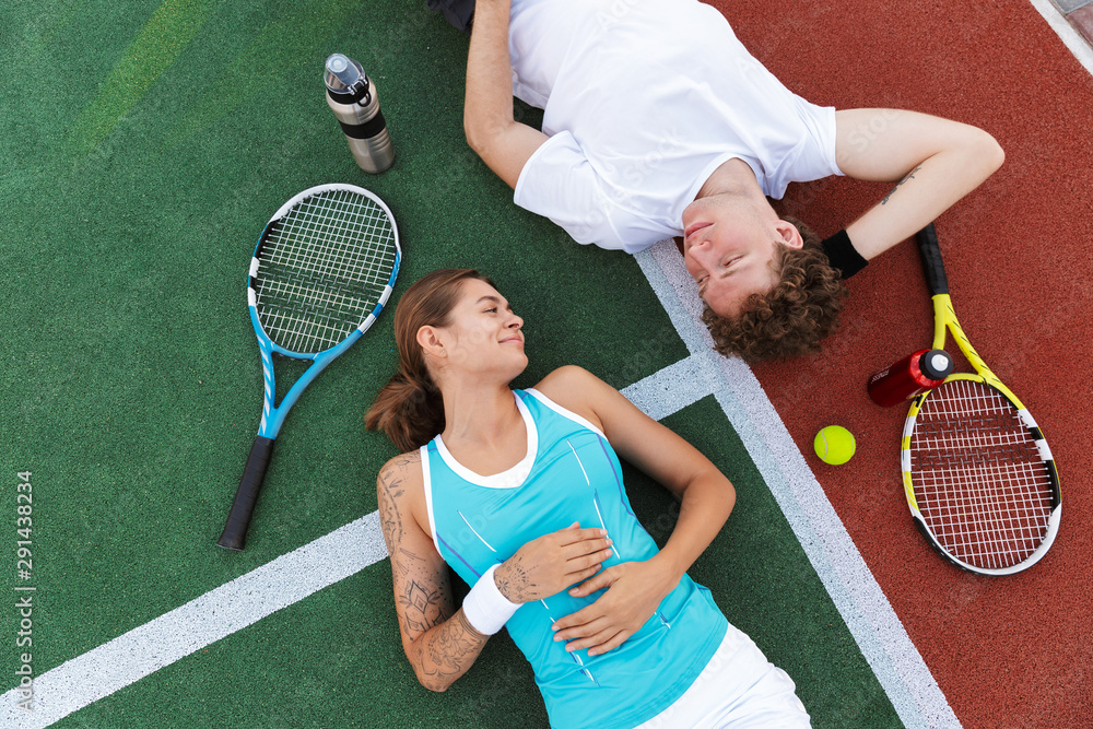 Image of athletic man and woman lying on court while playing tennis