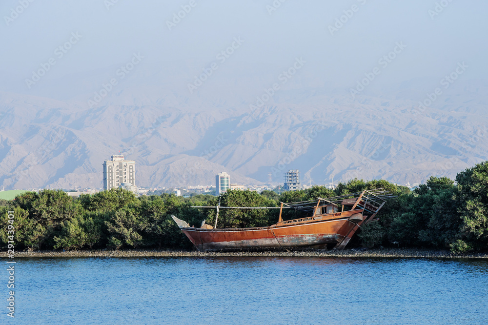 Panorama of Ras Al Khaimah, UAE .Lonely dhow traditional boat with sun lit mountains in the background. View from the corniche