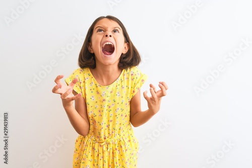 Cuadro en lienzo Young beautiful child girl wearing yellow floral dress standing over isolated white background crazy and mad shouting and yelling with aggressive expression and arms raised