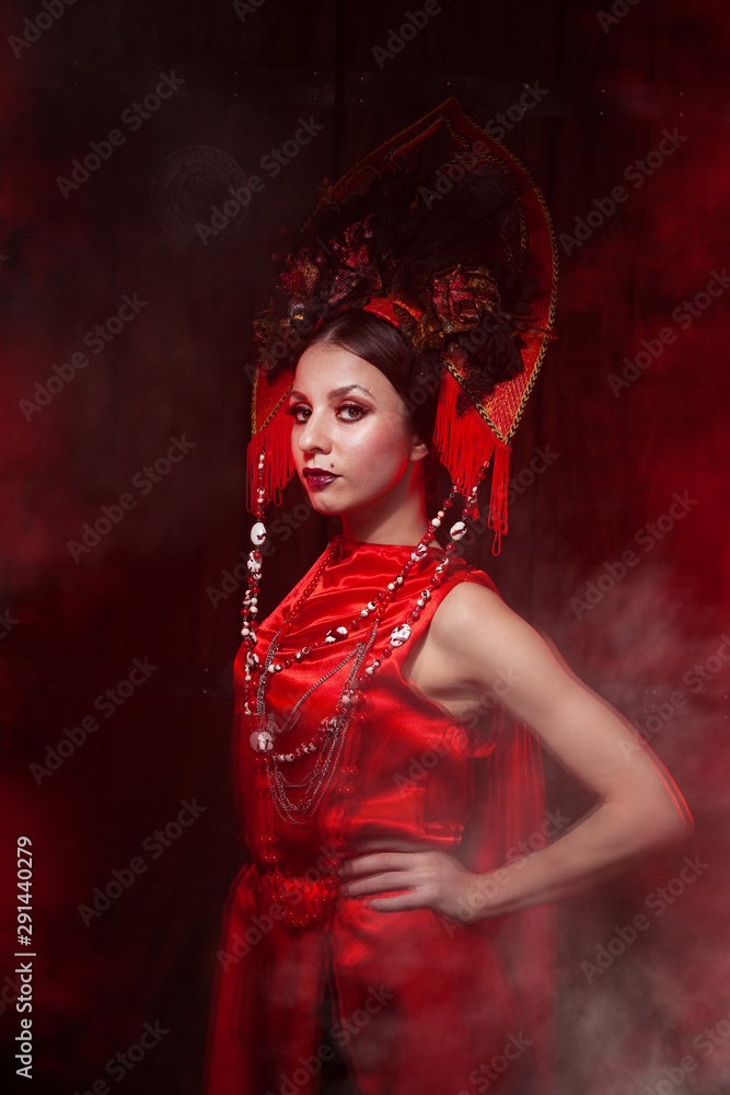 strict stylish girl in a fashionable long red dress and a voluminous hat on the background of smoke in the Studio at night alone. Halloween concept. strict stylish girl in a fashionable long red dress and a voluminous hat on the background of smoke in the Studio at night alone. Halloween concept.