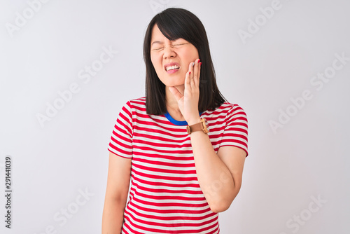 Young beautiful chinese woman wearing red striped t-shirt over isolated white background touching mouth with hand with painful expression because of toothache or dental illness on teeth © Krakenimages.com