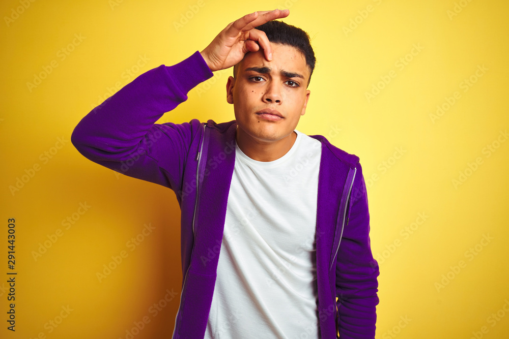 Young brazilian man wearing purple sweatshirt standing over isolated yellow background pointing unhappy to pimple on forehead, ugly infection of blackhead. Acne and skin problem Young brazilian man wearing purple sweatshirt standing over isolated yellow background pointing unhappy to pimple on forehead, ugly infection of blackhead. Acne and skin problem
