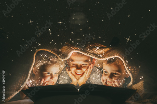 children reading a book under a blanket with light