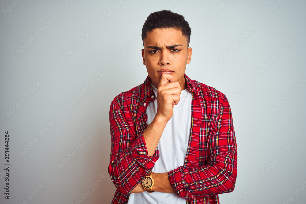 Young brazilian man wearing red shirt standing over isolated white background looking confident at the camera smiling with crossed arms and hand raised on chin. Thinking positive. Young brazilian man wearing red shirt standing over isolated white background looking confident at the camera smiling with crossed arms and hand raised on chin. Thinking positive.