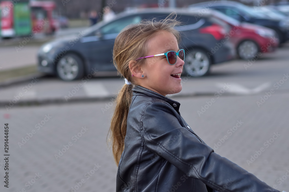 Laughing girl in a leather jacket and sunglasses on the street