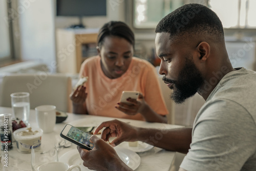 Fotografie Young African American couple distracted from breakfast by their cellphones