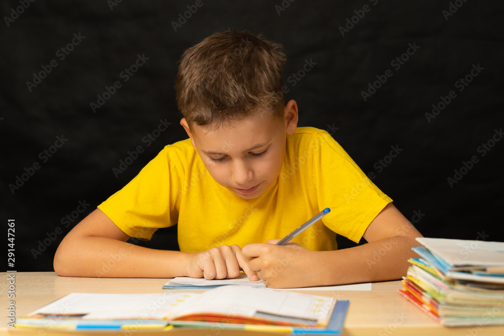 The boy solves homework, sitting at his desk. The boy writes homework with his left hand The boy solves homework, sitting at his desk. The boy writes homework with his left hand