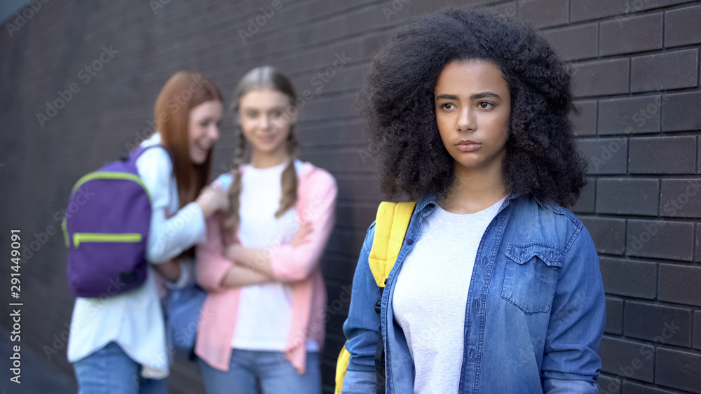 Two female students laughing at curly afro-american teenager, school bullying