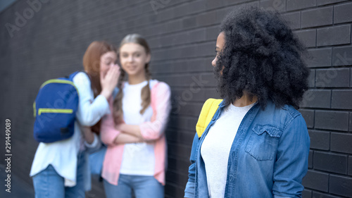 Slika na platnu Afro-american female student looking at gossiping classmates behind, college