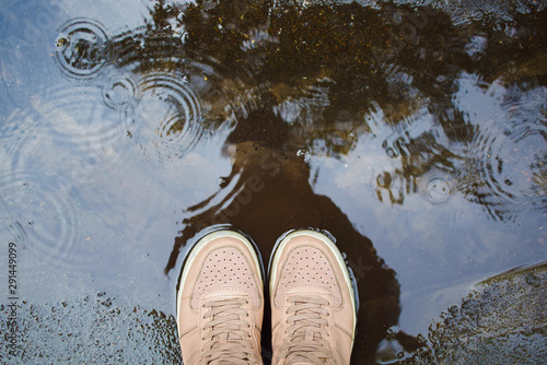 Canvas Print female legs in sneakers stand in a rain puddle