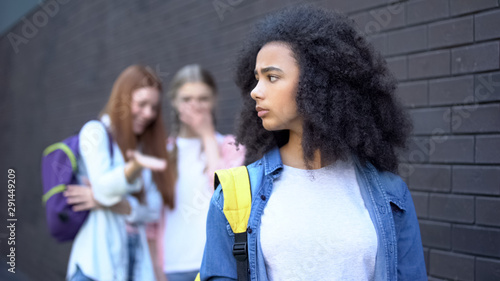 Tablou pe pânză Confused black schoolgirl front mocking college teenagers, laughing classmates