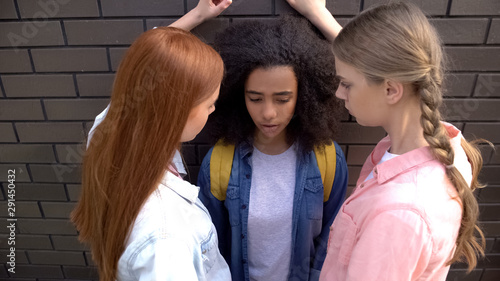 Two caucasian schoolgirls intimidating afro-american classmate, teen cruelty