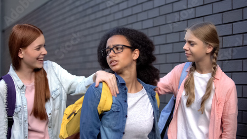 Fotografie College students stopping frightened black teenager in school backyard, bullying