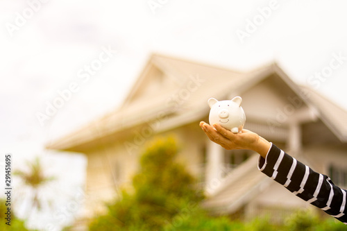 Small piggy bank in woman hand front of house. - saving and buy house and real estate concept.