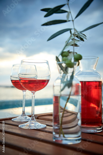 two glasses of rose wine with olives against blue water on a pier..