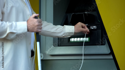 Fotografie Blind man searching audio jack in talking atm, using headset to withdraw money