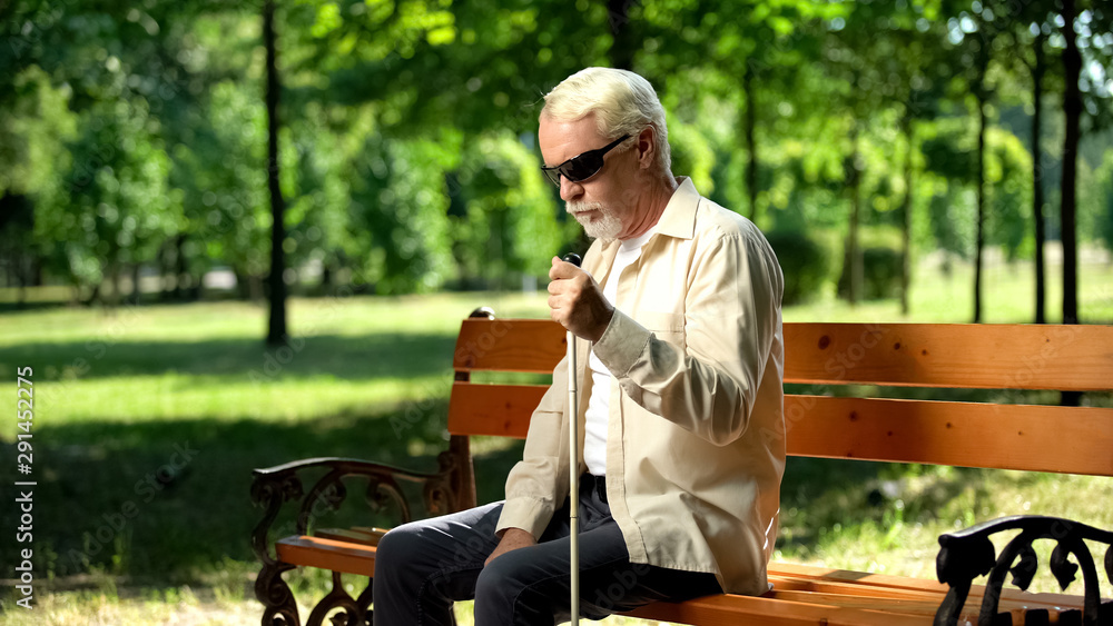 Depressed blind man sitting alone in park, socially disadvantaged population