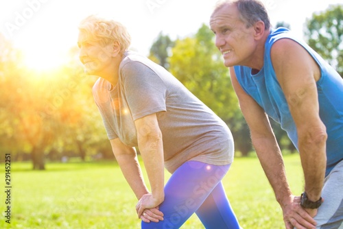 Active senior couple stretching in park with yellow lens flare in background