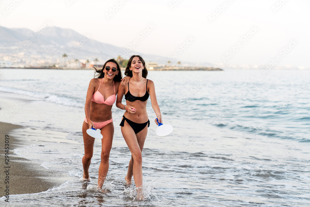 Girlfriends walking in embrace on foamy seashore