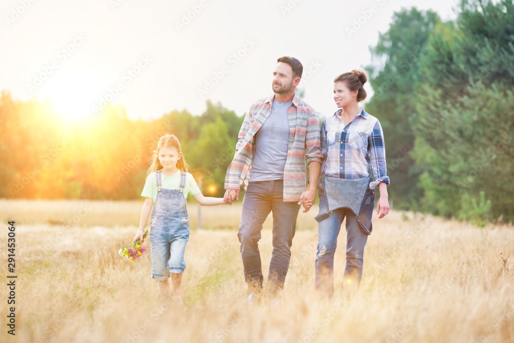 Happy family walking in wheat field with yellow lens flare in background