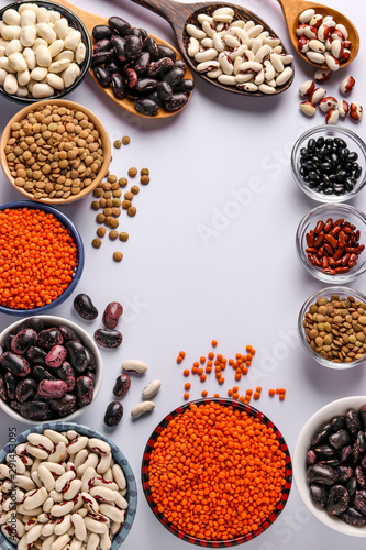 Red and brown lentils, black, brown and white beans are legumes that contain a lot of protein are located in bowls on white background, concept is healthy eating, copy space, vertical orientation