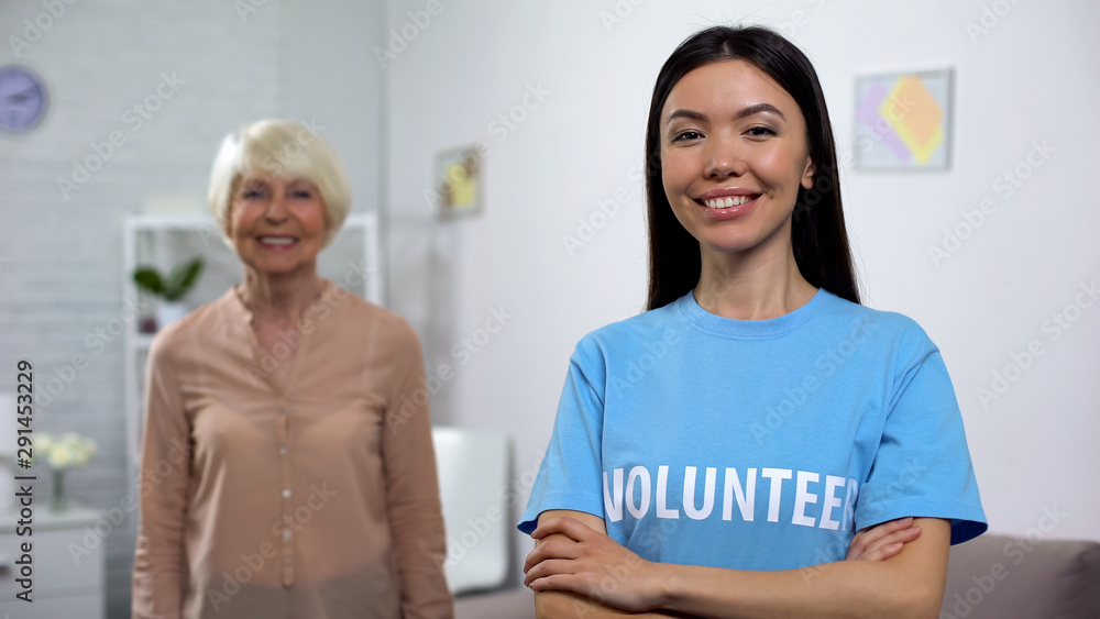 Smiling young volunteer with happy old lady on background, social protection Smiling young volunteer with happy old lady on background, social protection