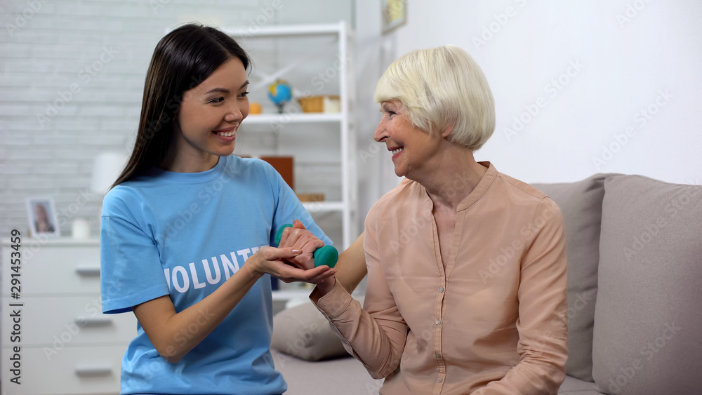 Fototapeta premium Social worker assisting old woman making exercise with dumbbell, rehabilitation