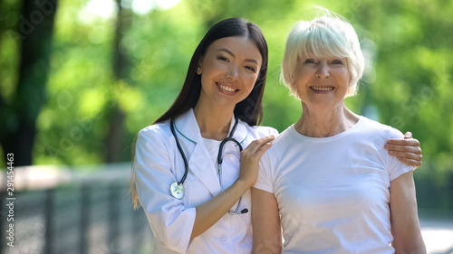 Nurse hugging happy senior woman and smiling into camera, day in hospital park © motortion