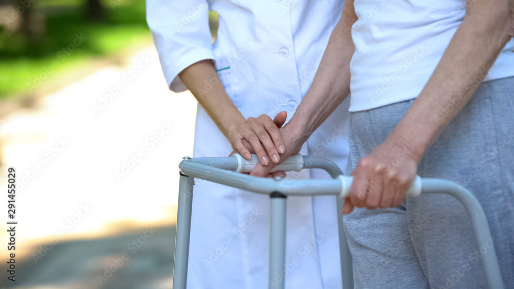 Female doctor holding hand of woman walking with frame, supporting in rehab