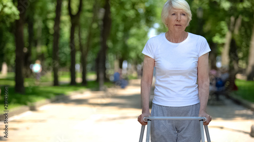 Sad disabled woman with frame walking in park, rehabilitation after trauma