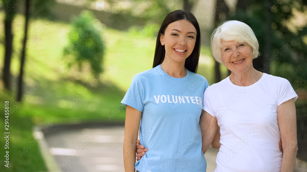 Cheerful old woman and young female volunteer smiling on camera, charity support Cheerful old woman and young female volunteer smiling on camera, charity support