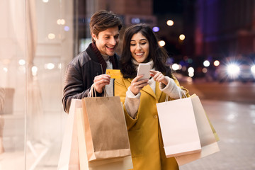 Consumerism concept. Happy couple checking cellphone outdoors