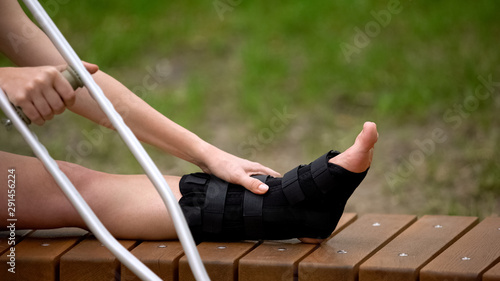 Bilde på lerret Woman with ankle brace holding crutch sitting outdoors, trauma bandage, health