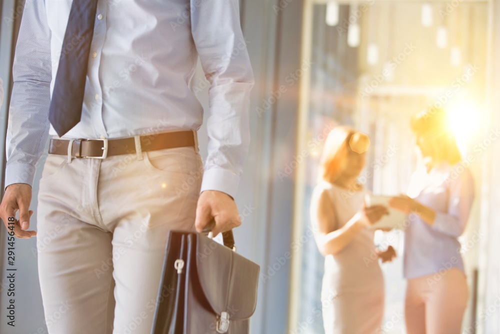 Obraz premium Cropped image of businessman carrying briefcase bag in office hall with yellow lens flare in background