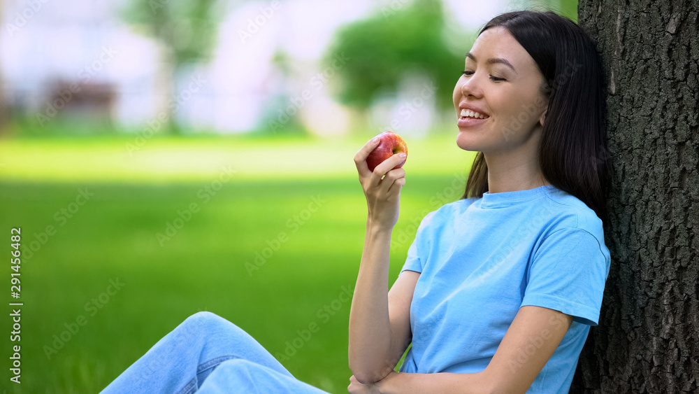 Asian pretty female holding fresh apple sitting outdoor, healthy snack, vitamins Asian pretty female holding fresh apple sitting outdoor, healthy snack, vitamins