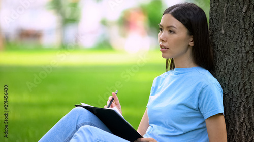 Thoughtful female writer sitting garden with pen, working journalist inspiration