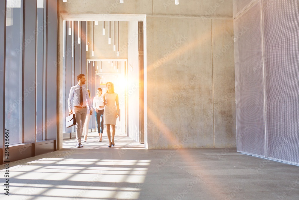 Business people walking in office hall with yellow lens flare in background - obrazy, fototapety, plakaty 