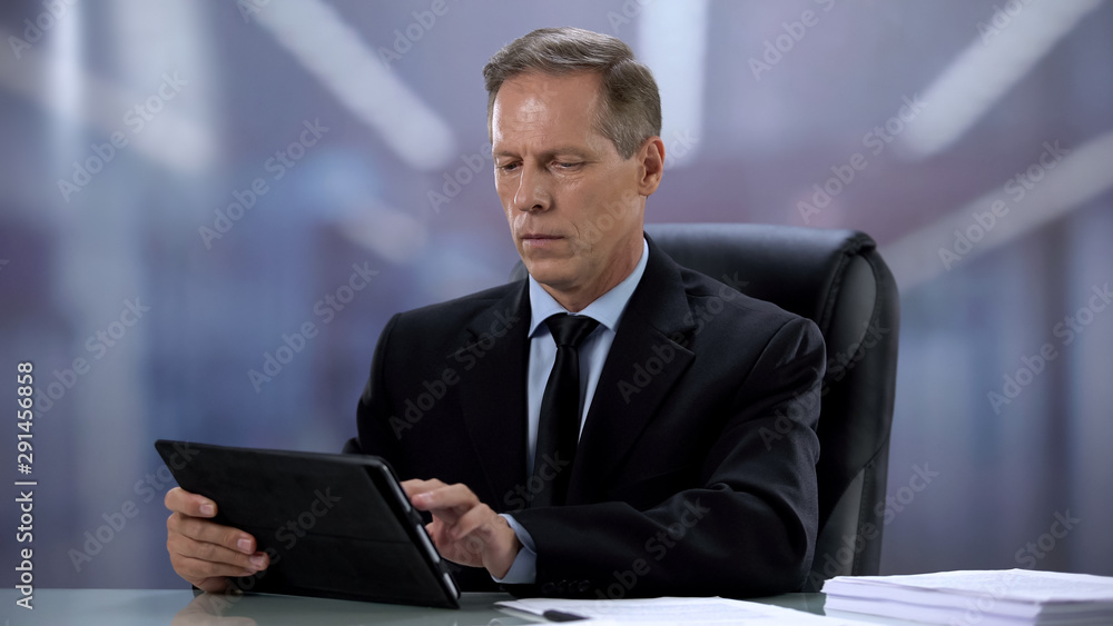 Confident male boss working on tablet pc at office desk, online documentation