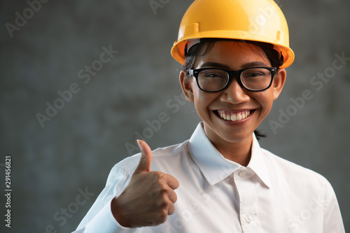 Portrait of smiling Asian woman engineer showing thumbs up gesture over concrete wall background