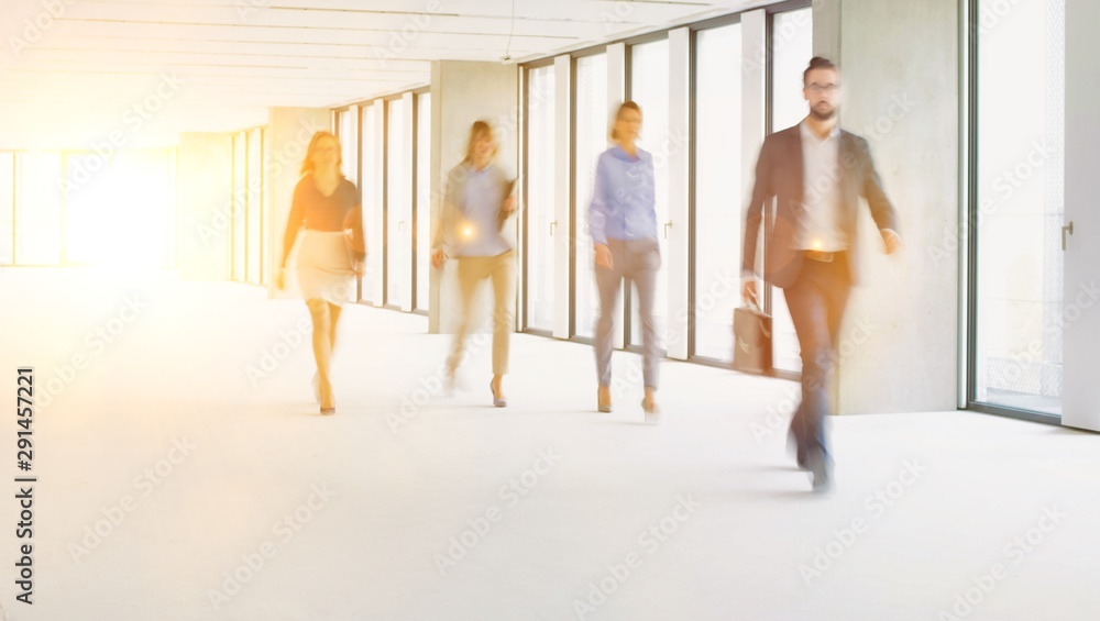 Business people walking in office corridor with yellow lens flare in background