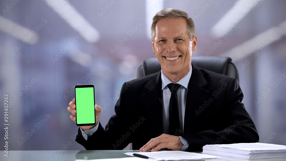 Joyful male boss in suit showing green screen smartphone at camera, business app Joyful male boss in suit showing green screen smartphone at camera, business app