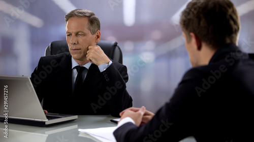 Employer looking at laptop screen listening young candidate during job interview